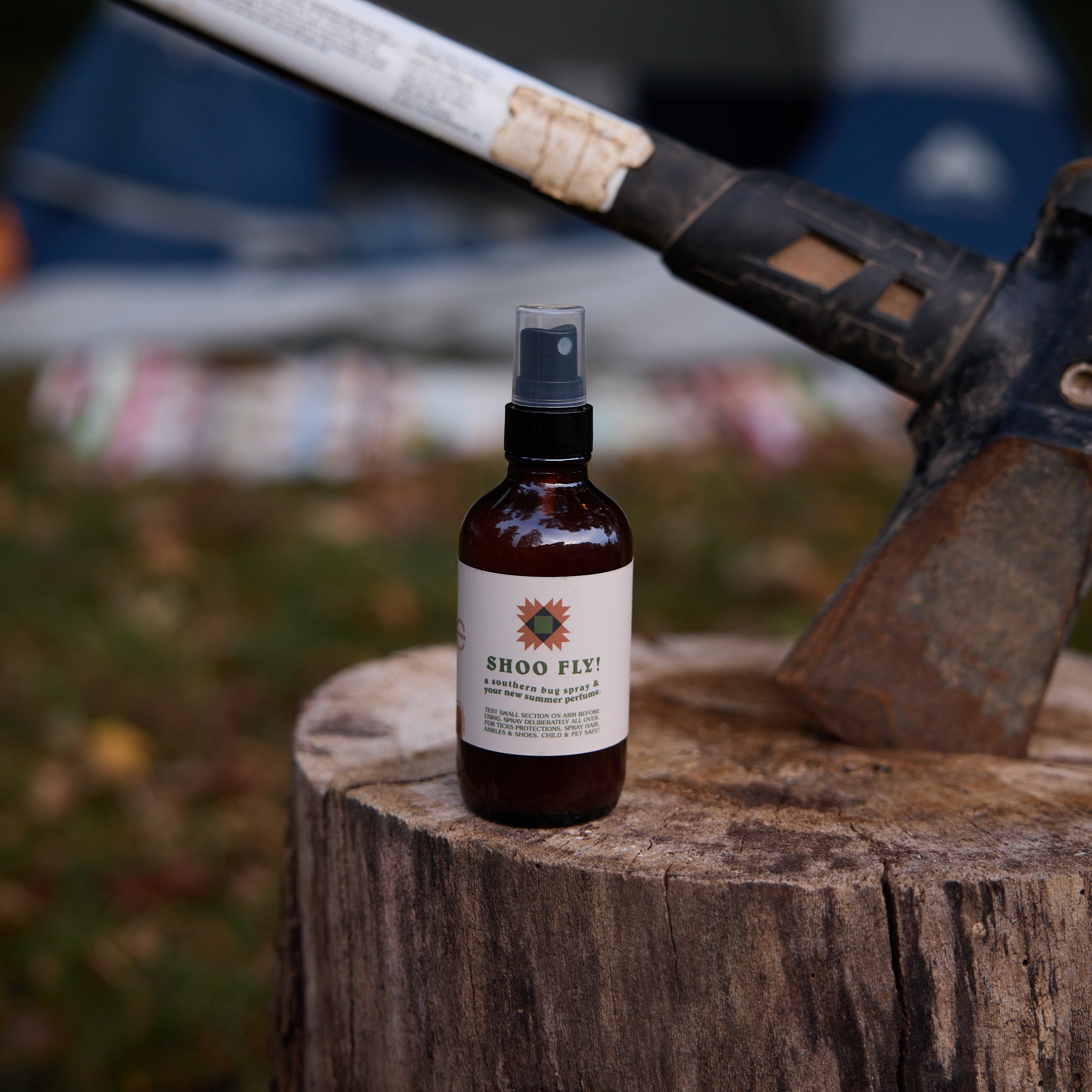 Shoo Fly bug spray bottle sits on a tree stump next to a camping axe for outdoor protection.
