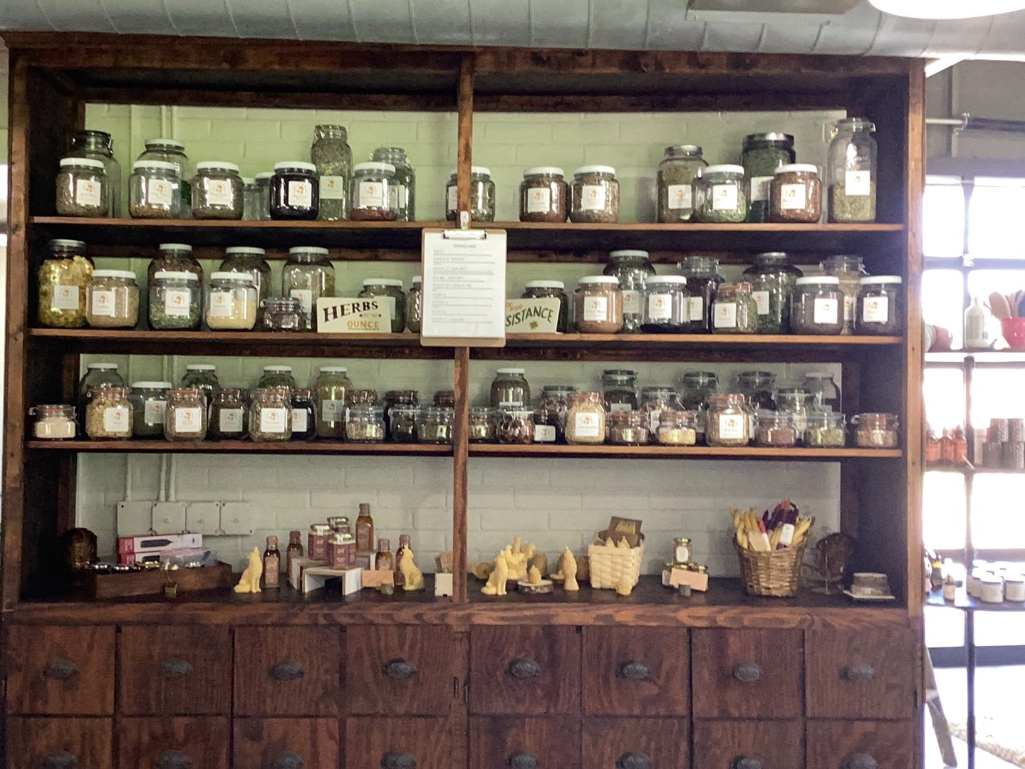 A rustic wooden apothecary cabinet displays numerous jars of herbs, spices, and handmade goods for sale.
