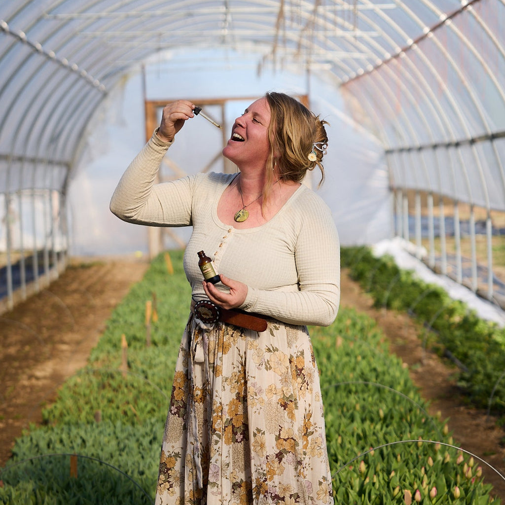 Woman standing in a greenhouse holding comfort tincture by cedar hill homestead.