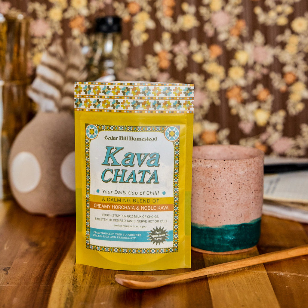 Kava Chata powdered drink mix package on a wooden table with a floral-patterned curtain in the background