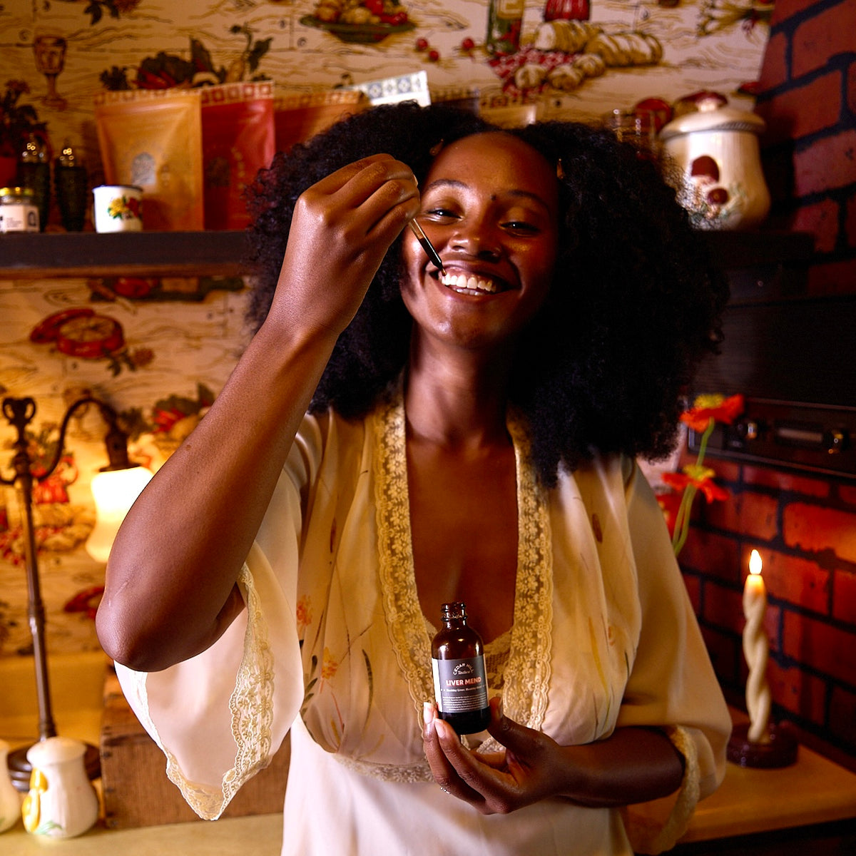 Smiling woman applies Liver Mend tincture with a dropper in a cozy, vintage kitchen setting.
