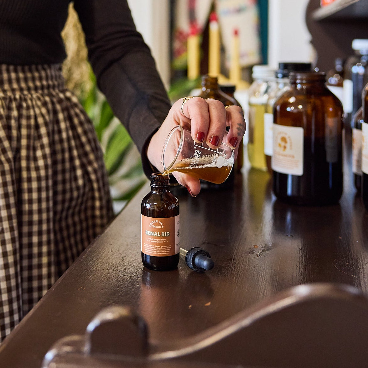 Person pouring liquid from a glass bottle into a dropper bottle on a counter.