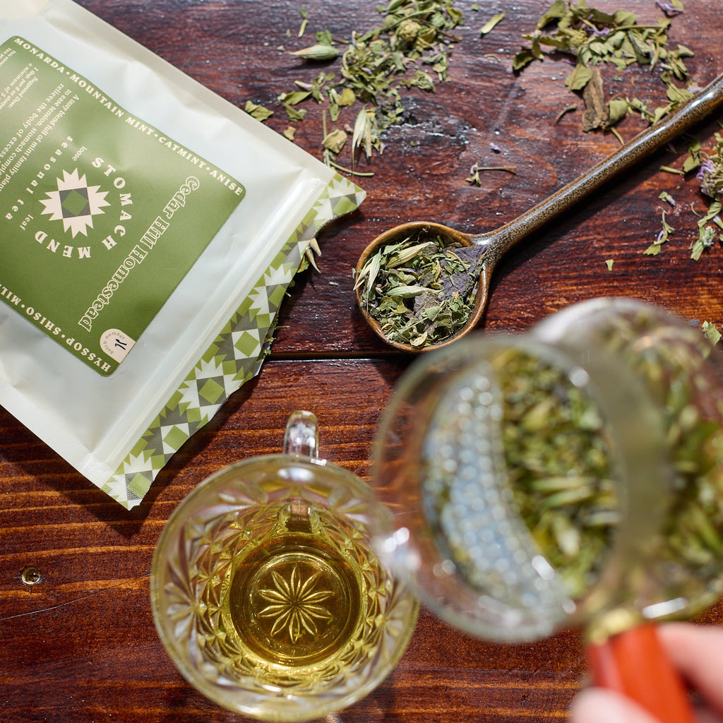 Tea leaves on a wooden surface with a tea bag and cup.