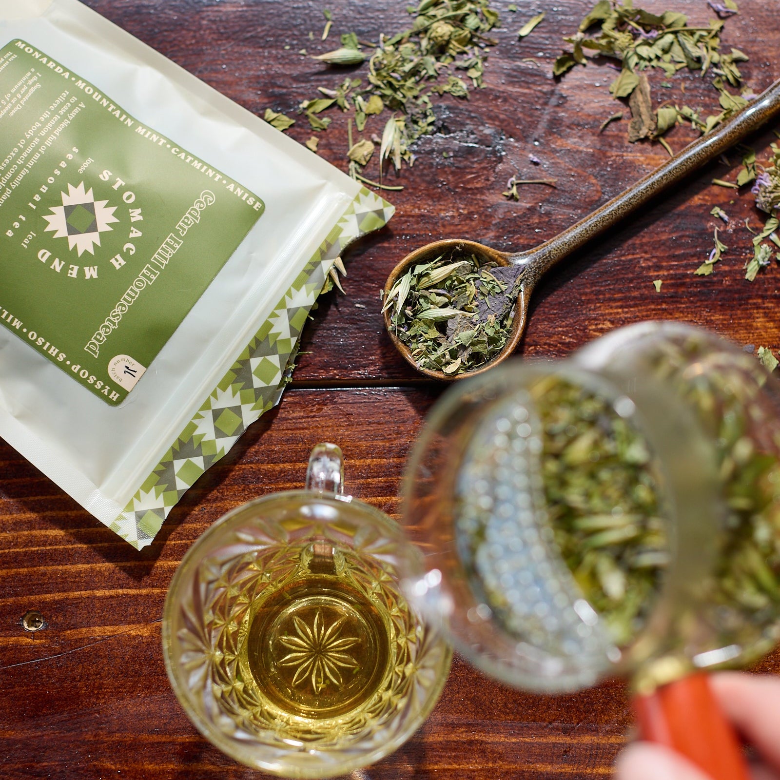Tea leaves on a wooden surface with a tea bag and cup.